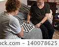 Elderly couple plays checkers together on a gray couch in their living room 140078625