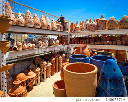 Gata de Gorgos, SPAIN - May 20, 2026.The outdoor pottery market features shelves filled with various handmade terracotta planters, decorative blue pots, and clay lanterns. The bright sun highlights th 140078714