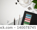 Top view of office supplies on a white desk. Black notebook with colorful sticky tabs, pencils, a cutting mat, tape dispenser, and paper clips. Copyspace 140078745