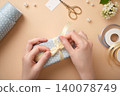 Hands are tying a bow on a light blue box. The process of wrapping a present. 140078749