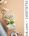 Gift box in light blue polka dot paper with cream satin ribbon, white lilac flowers, blank tag, gold scissors and pearls on beige background. Copyspace 140078750