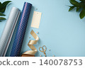 Gift wrapping accessories with polka dot paper rolls, ribbon, blank tag, scissors, pearls and green leaves on blue background. Copyspace 140078753