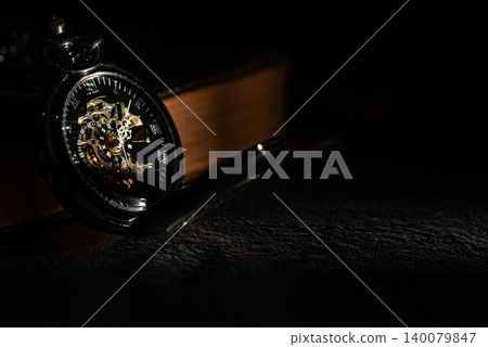 Antique pocket watch, a beautiful low-key scene of a wonderful pocket watch illuminated by a sliver of light from a window, selective focus. Antique pocket watch, a beautiful low-key scene of a wonderful pocket watch illuminated by a sliver of light from a window, selective focus. 140079847