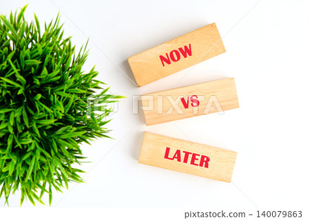 Three wooden blocks spell out NOW VS LATER, arranged vertically on a bright white surface Three wooden blocks spell out NOW VS LATER, arranged vertically on a bright white surface 140079863