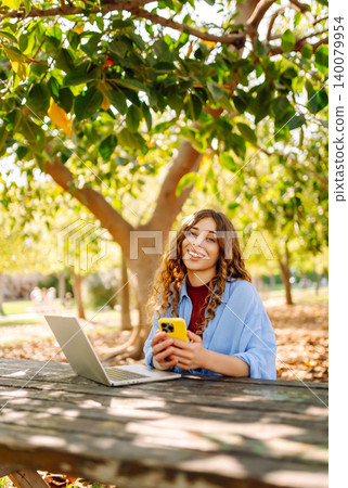Happy woman with laptop and phone at table in an outdoor near lake. Business, blogging, freelancing. 140079954