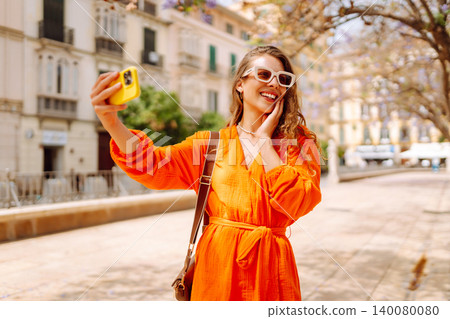 Happy attractive young woman posing to camera make selfie smiling at sunlight on street. Travel Happy attractive young woman posing to camera make selfie smiling at sunlight on street. Travel 140080080