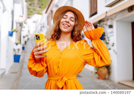 Young woman to take a quick selfie as a souvenir of her trip in a sunny village. Tourist Adventure 140080197