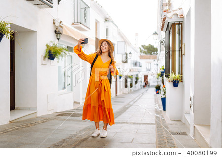 Young woman to take a quick selfie as a souvenir of her trip in a sunny village. Tourist Adventure Young woman to take a quick selfie as a souvenir of her trip in a sunny village. Tourist Adventure 140080199
