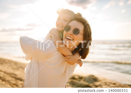 A mother and daughter enjoy a sunny beach stroll, as waves gently lap at their feet during sunset A mother and daughter enjoy a sunny beach stroll, as waves gently lap at their feet during sunset 140080331