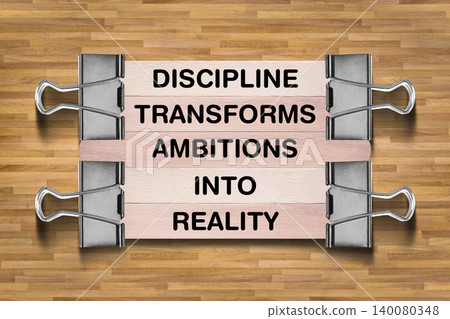 Discipline Transforms Ambitions Into Reality tagline written on wooden stick hold by binder clip with wooden texture background, business and investment, stock market theme 140080348