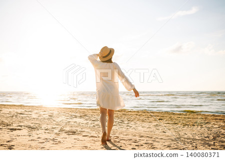 Young woman walking by beach at golden sunset - Female tourist on summer vacation. Young woman walking by beach at golden sunset - Female tourist on summer vacation. 140080371