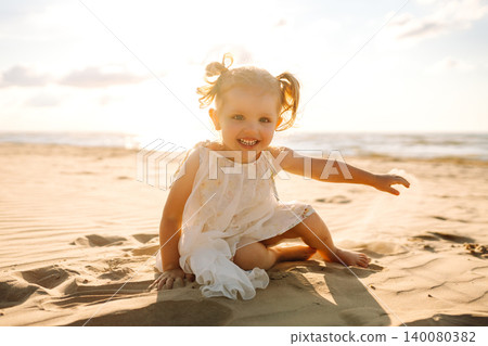 Little girl plays joyfully along the sandy beach during a sunny day by the ocean Little girl plays joyfully along the sandy beach during a sunny day by the ocean 140080382
