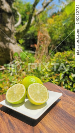 Freshly cut limes and whole limes are served on a white plate against a backdrop of beautiful new greenery. Freshly cut limes and whole limes are served on a white plate against a backdrop of beautiful new greenery. 140080725