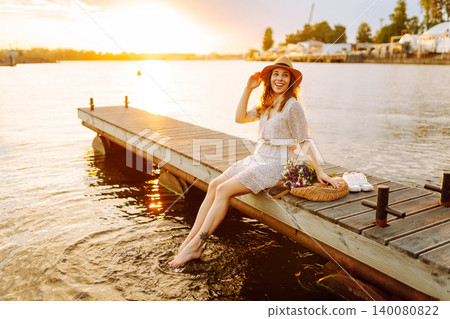 Young woman in dress sitting on wooden pier near pond. Rustic style of wedding. Travel, tourism 140080822