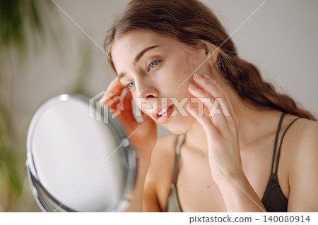 Young woman with problem skin looking into mirror. Inflammation on face, problem skin. Beauty care. 140080914