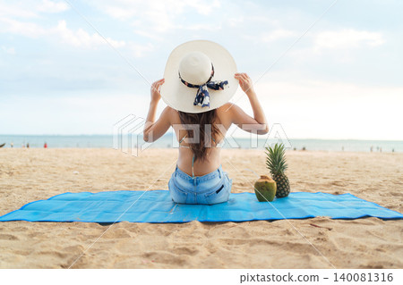 Happy Asian woman sitting on beach mat enjoying summer vacation Happy Asian woman sitting on beach mat enjoying summer vacation 140081316