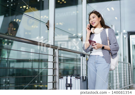 Happy Asian woman talking on smartphone at airport terminal Happy Asian woman talking on smartphone at airport terminal 140081354