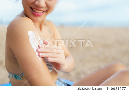 Asian woman applying sunscreen on shoulder at the beach Asian woman applying sunscreen on shoulder at the beach 140081377
