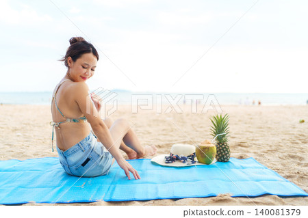 Asian woman applying sunscreen on shoulder at the beach Asian woman applying sunscreen on shoulder at the beach 140081379