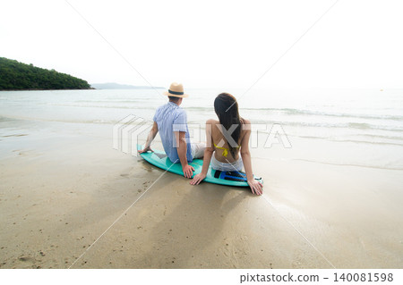 Young Couple Sitting on Surfboard Watching the Ocean at Beach Young Couple Sitting on Surfboard Watching the Ocean at Beach 140081598