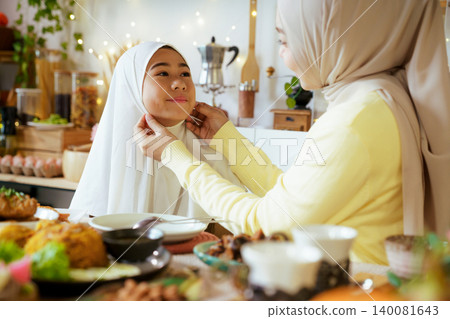 Muslim Mother Adjusting Daughter Hijab Before Ramadan Iftar Meal Muslim Mother Adjusting Daughter Hijab Before Ramadan Iftar Meal 140081643