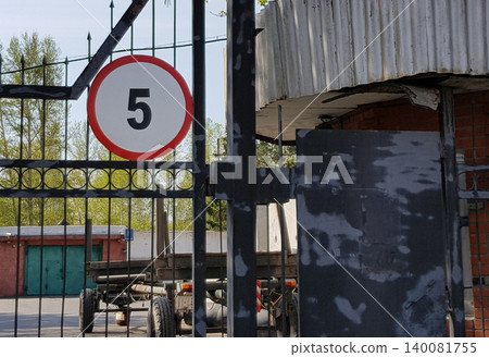 Guarded entrance to the industrial garage parking area, surrounded by a steel fence. There is a sign on the gate that limits the speed to 5 km Guarded entrance to the industrial garage parking area, surrounded by a steel fence. There is a sign on the gate that limits the speed to 5 km 140081755