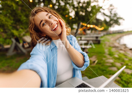Selfie portrait of young woman with laptop at a table in nature. Concept of technology, freelancing. Selfie portrait of young woman with laptop at a table in nature. Concept of technology, freelancing. 140081825