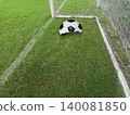 Deflated soccer ball on green grass field near the goal post, failure or missed opportunity concept 140081850