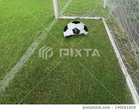 Deflated soccer ball on green grass field near the goal post, failure or missed opportunity concept 140081850