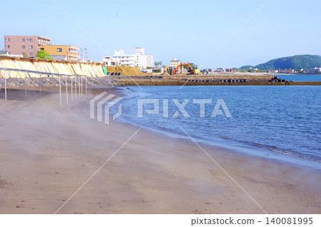A photograph of the beach near a hot spring bath with steam rising in the early morning. A photograph of the beach near a hot spring bath with steam rising in the early morning. 140081995