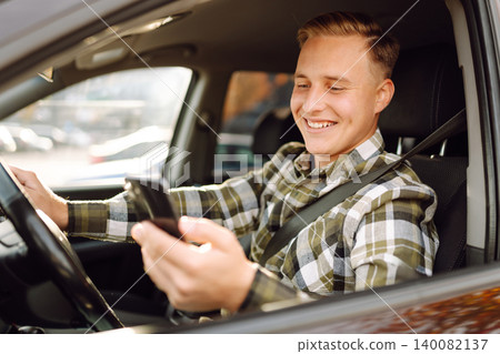 Man using smartphone while sitting in car parked in urban area during daytime. Lifestyle concept. 140082137