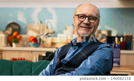 Portrait of male pensioner with candid smile resting at home on couch, domestic life alone with relaxation and tranquility. Senior man feeling peaceful during quiet retirement moments, aging. Portrait of male pensioner with candid smile resting at home on couch, domestic life alone with relaxation and tranquility. Senior man feeling peaceful during quiet retirement moments, aging. 140082158