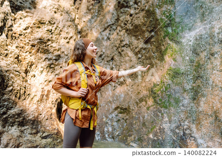 Smiling female dressed in hiking clothes, enjoys a waterfall near a mountain river. Travel, trekking Smiling female dressed in hiking clothes, enjoys a waterfall near a mountain river. Travel, trekking 140082224
