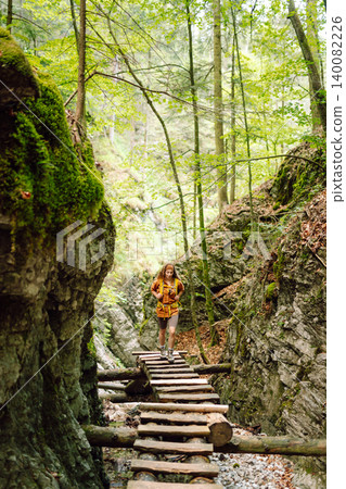 A woman traveler with a bright backpack travels through the mountains on a hiking trail. Adventures. A woman traveler with a bright backpack travels through the mountains on a hiking trail. Adventures. 140082226