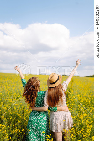 Two young happy women in middle of a yellow rapeseed field. Concept of fun, relaxation. Lifestyle. Two young happy women in middle of a yellow rapeseed field. Concept of fun, relaxation. Lifestyle. 140082287