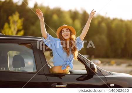 Smiling woman from the window of the car enjoys natureCar travel, sunset light. Active lifestyle. Smiling woman from the window of the car enjoys natureCar travel, sunset light. Active lifestyle. 140082630