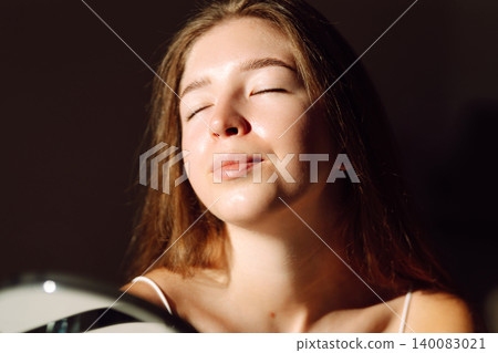 Young woman reflected in the mirror in soft evening light in a cozy room. Beauty and care concept. Young woman reflected in the mirror in soft evening light in a cozy room. Beauty and care concept. 140083021