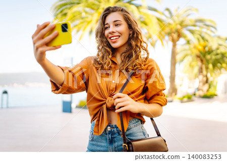 Happy woman with a phone in her hands blogs, takes a selfie on a sunny day. Tourism concept. Happy woman with a phone in her hands blogs, takes a selfie on a sunny day. Tourism concept. 140083253