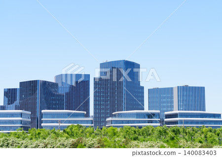 現代化的藍色玻璃幕牆辦公大樓、綠樹成蔭,以及城市的藍色天際線。 現代化的藍色玻璃幕牆辦公大樓、綠樹成蔭,以及城市的藍色天際線。 140083403