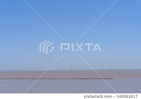 離岸風力發電廠:地平線上聳立渦輪機,藍天下潮灘帶來清潔能源。 離岸風力發電廠:地平線上聳立渦輪機,藍天下潮灘帶來清潔能源。 140083617