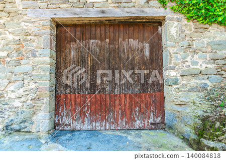 Weathered wooden garage door in rustic stone building facade of medieval Rupit village, Catalonia, Spain 140084818