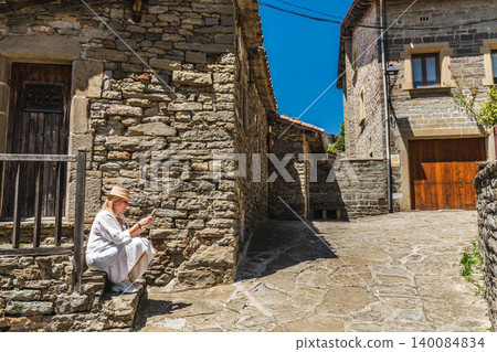 Woman using smartphone while resting in medieval stone village of Rupit, Catalonia, Spain, sitting on historic street Woman using smartphone while resting in medieval stone village of Rupit, Catalonia, Spain, sitting on historic street 140084834