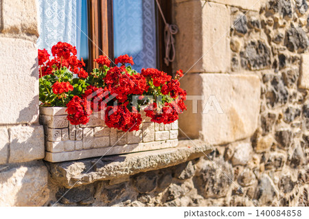 Window with vibrant red geranium flowers on stone house facade in traditional Catalan village Window with vibrant red geranium flowers on stone house facade in traditional Catalan village 140084858