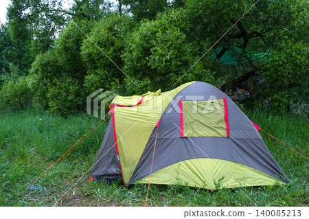 Large yellow and grey tent among trees, forest campsite, outdoor adventure area for tourism, picturesque travel scene, family or group camping. Large yellow and grey tent among trees, forest campsite, outdoor adventure area for tourism, picturesque travel scene, family or group camping. 140085213