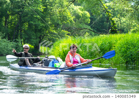 Senior couple on a Varzuga kayak, nature paddling adventure, mature travel, green riverbank, wellness and harmony. Senior couple on a Varzuga kayak, nature paddling adventure, mature travel, green riverbank, wellness and harmony. 140085349