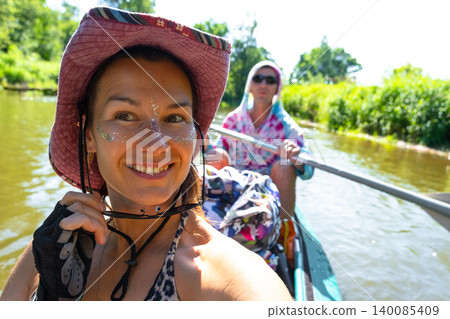 Woman paddling kayak on river, making selfie, summer water tourism, active lifestyle, recreation gear, boating adventure. 140085409