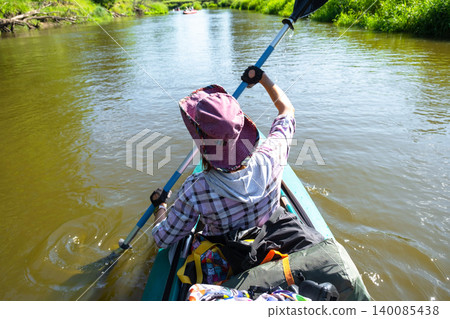 Woman in a kayak paddling on river, sporting hat, summer adventure, outdoor activity, nature tourism and water gear use. 140085438