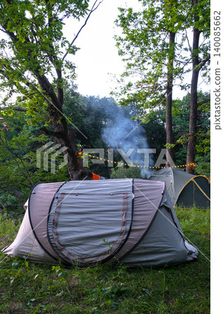 Tent with rising smoke in summer forest campsite, tourism, rural landscape, recreational travel and adventure camping scene. Tent with rising smoke in summer forest campsite, tourism, rural landscape, recreational travel and adventure camping scene. 140085662