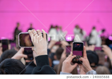 Audience members hold smartphones, record live stage performance against bright pink backdrop, creating dynamic concert atmosphere with focus on mobile viewing, event engagement. Audience, technology Audience members hold smartphones, record live stage performance against bright pink backdrop, creating dynamic concert atmosphere with focus on mobile viewing, event engagement. Audience, technology 140085688