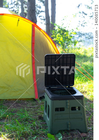 Open portable toilet in front of yellow tent, outdoor campsite sanitation, usage for comfort, hygiene, travel and tourism area. 140085713